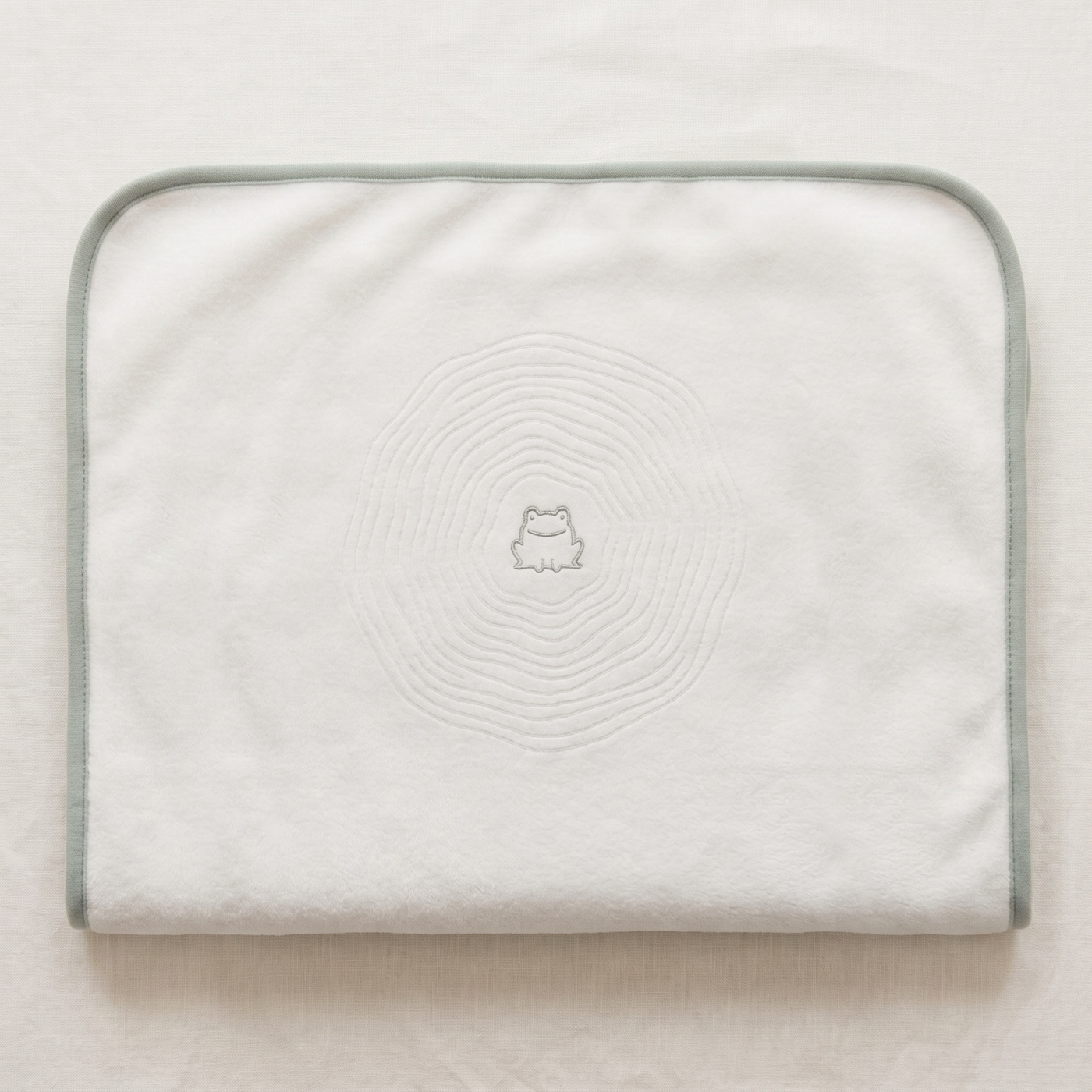 The lillypad neatly folded on linen, plush and thick, with the frog embroidery centered on top